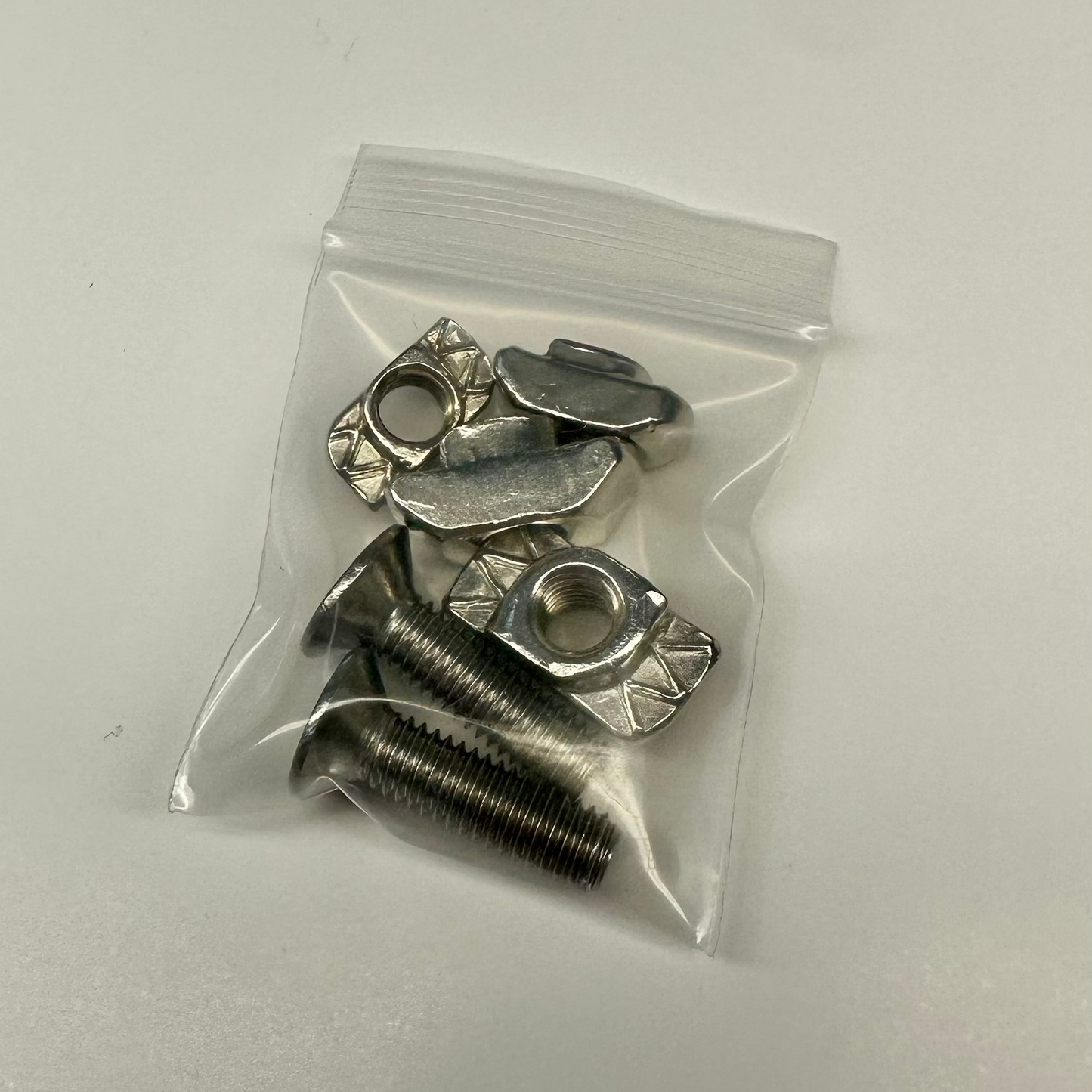 A small clear plastic bag containing stainless steel T-slot nuts and countersunk screws, typically used in aluminum extrusion systems, provided by Metalgear Engineering.